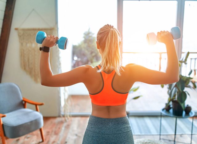 woman doing dumbbell shoulder press exercise in living room, concept of at-home workouts for beginners