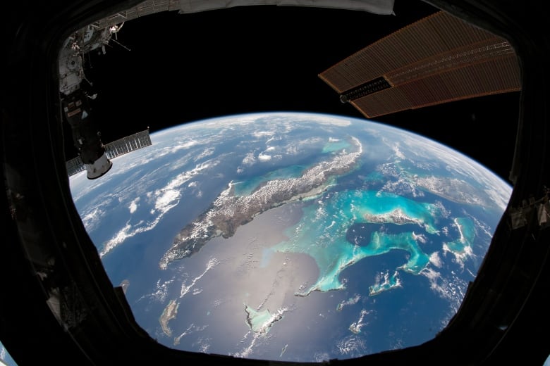 Through a window on the space station, we see blue sparkly ocean over the Caribbean Sea with small wisps of clouds around the Earth.