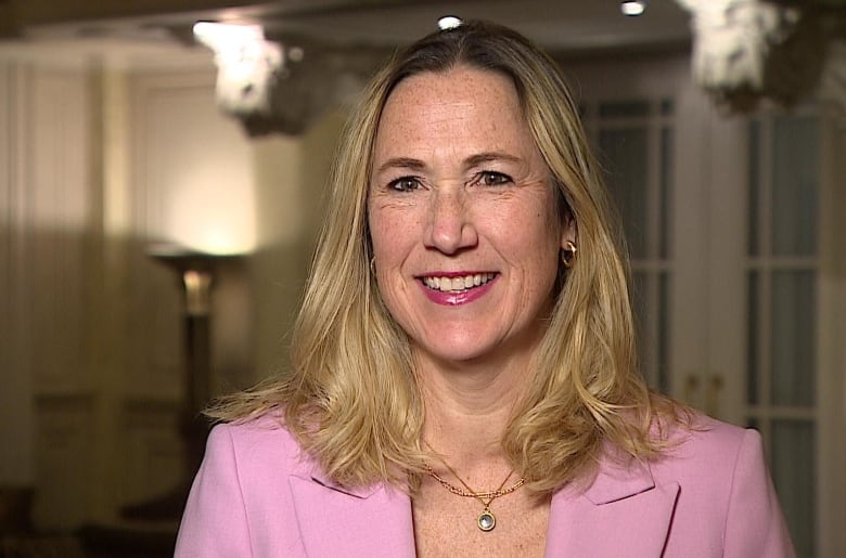 A blond woman wearing a pink blazer smiles. 