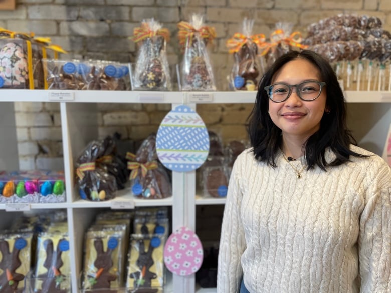 A woman smiles for a photo while posing in front of a shelf filled with chocolate treats.