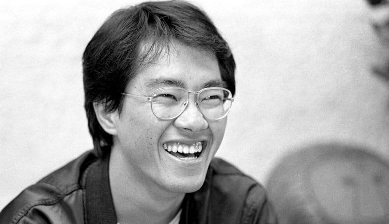 An Asian man wearing glasses and smiling is shown in closeup in a black and white photo that appears to have been taken in the distant past.