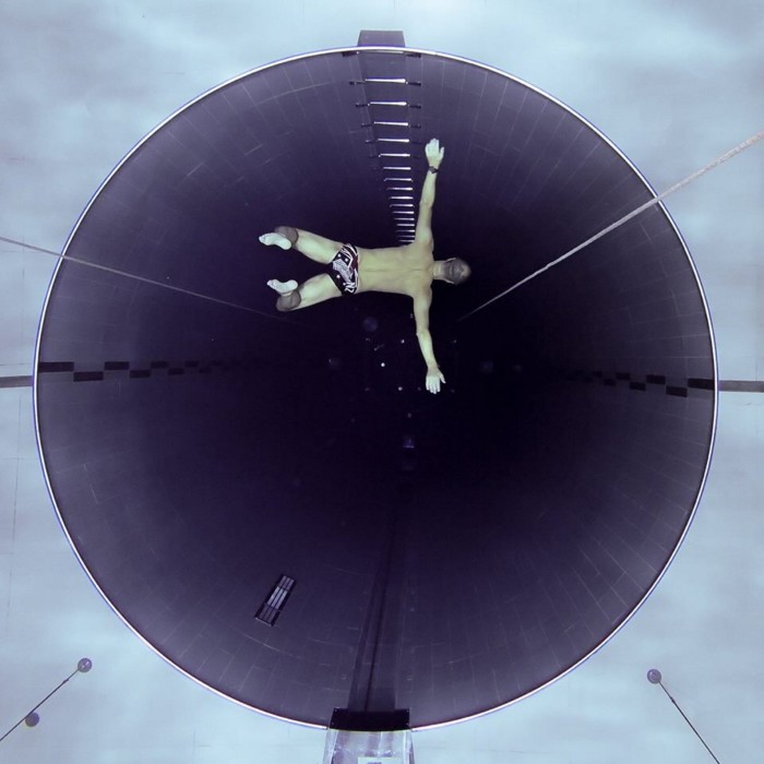 A swimmer lets himself fall into a deep cyclindrical hole at the bottom of a pool 