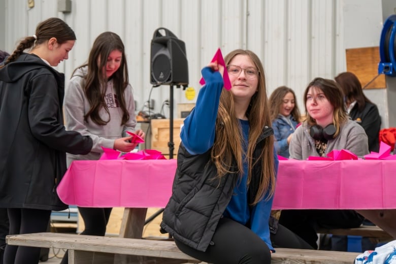 A young woman holds up a paper airplane and prepares to throw it. 