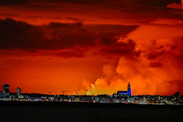 A city's nighttime skyline is pictured against the backdrop of an orange coloured sky and rising smoke.