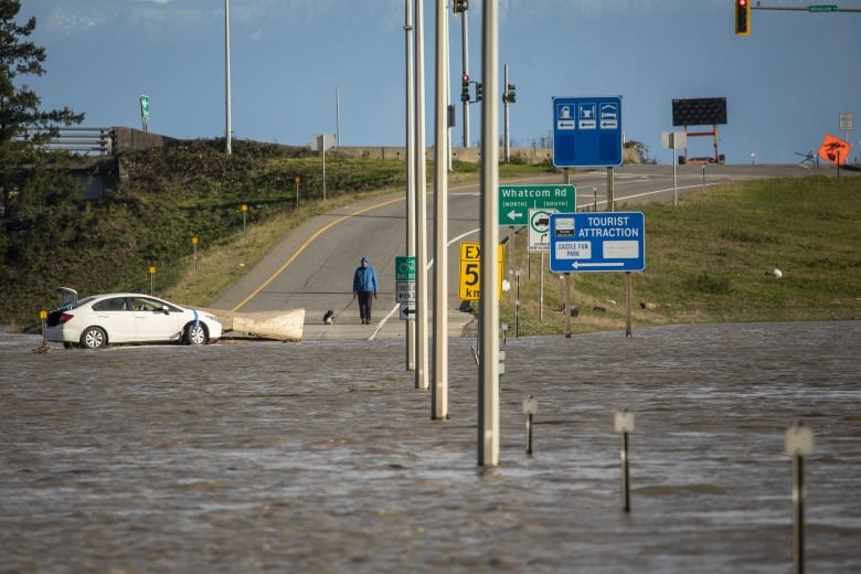 A road is submerged under floodwaters, with signs indicating tourist attractions and other roads around the corner.