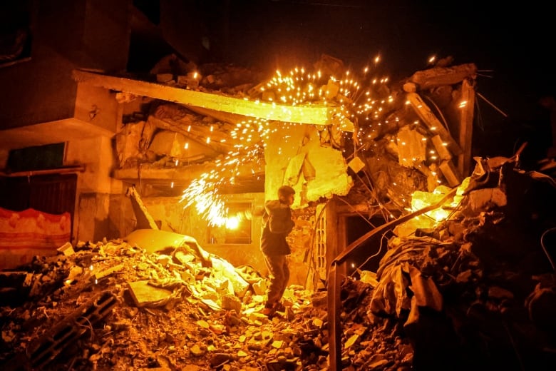 A child waves a sparkler firework amid the rubble of a destoryed building.