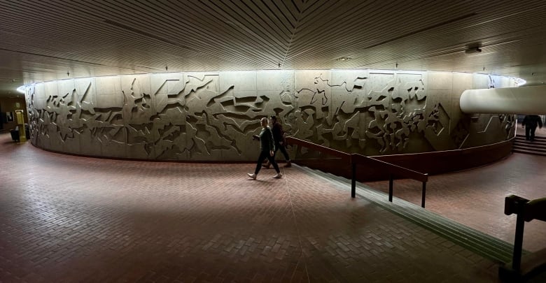 A pedestrian walking past the concrete sculpture below Portage and Main.