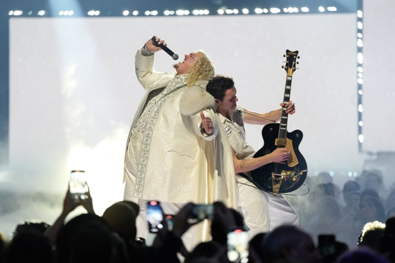 Two musicians stand back to back as they perform onstage. 