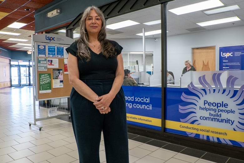 A person with long grey hair stands outside an office.