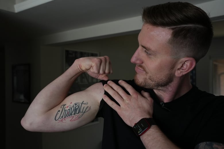 A person shows a tatoo saying "Travesty" on the right bicep.