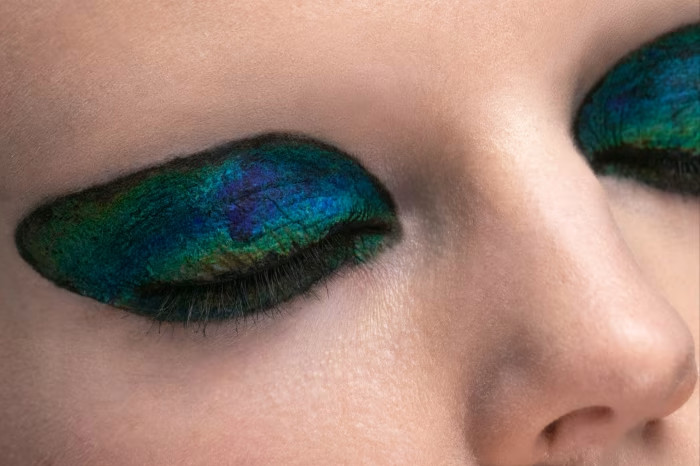 A close-up image of a model wearing green and blue eye shadow