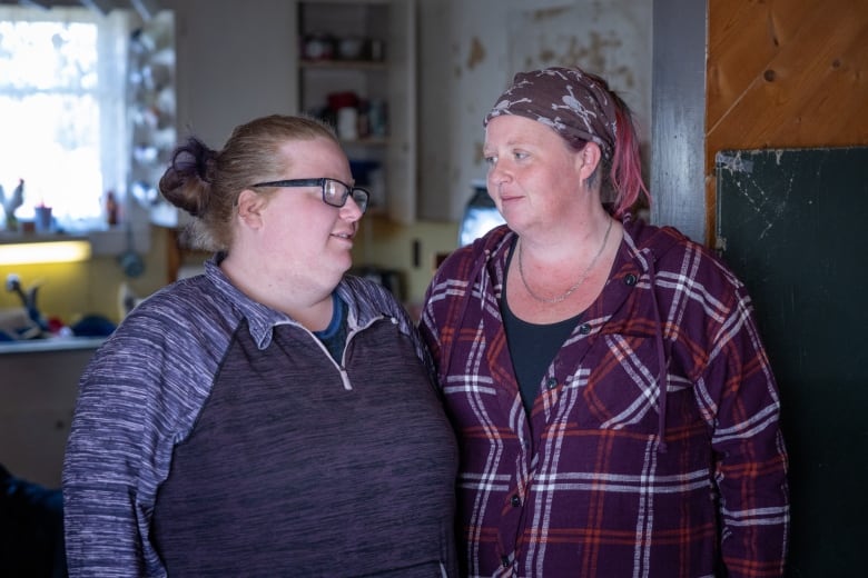 Two sisters are shown close together looking at each other in their family kitchen.