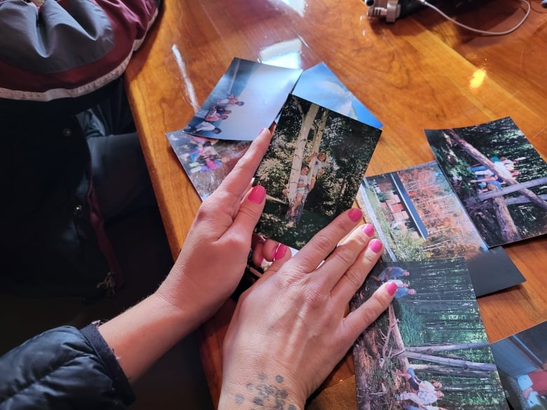 A woman's hands are seen looking at printed photographs of young girls taken in a park or forest, laid out on a table.