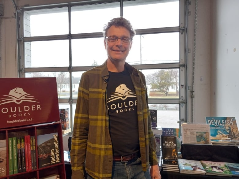 Man with curly grey hair standing next to display of books.