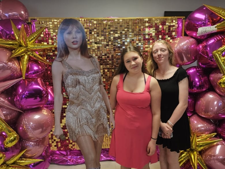 Two young women standing next to a carboard figure of the singer Taylor Swift.