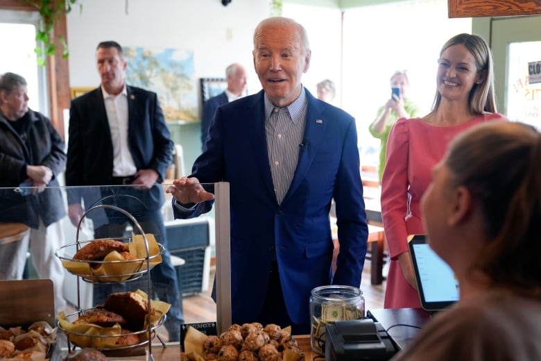 An elderly man in a blue suit reaches for some pastries. 