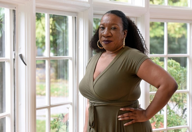 A woman in a  green dress stands in front of a window