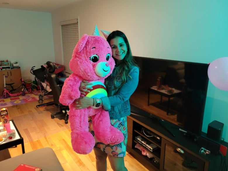 A woman holds a large pink stuffed bear.