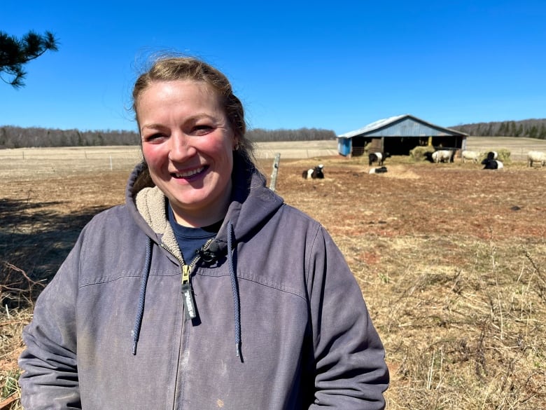 A woman smiles at the camera with a field of cows and a barn in the background.