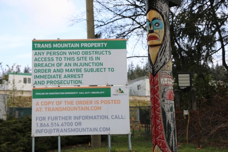 A totem pole is located beside a sign saying the property belongs to Trans Mountain.