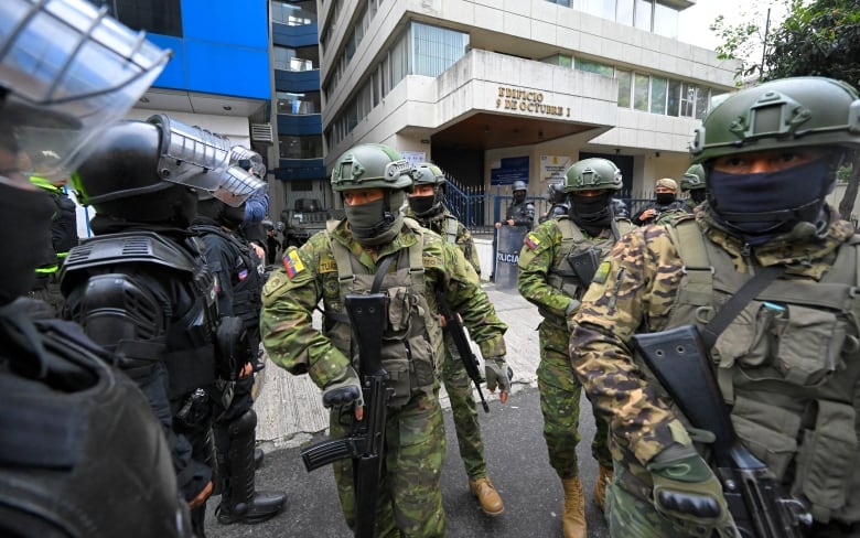 Armed police officers and military personnel gather outside a building.