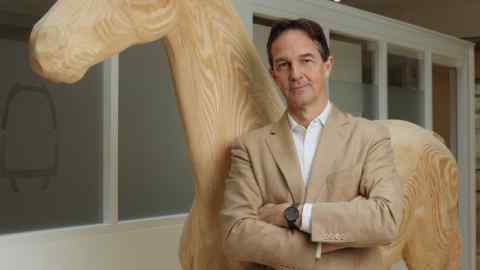 A man with his arms folded poses in front of a wooden horse