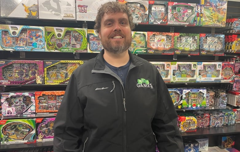 A man stands in front of store shelves stocked with Pokémon cards, packs and boxes.