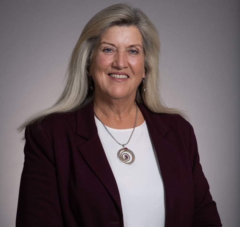 A woman smiles at the camera, wearing a burgundy blazer.