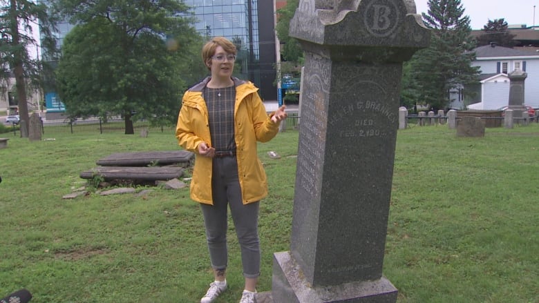 Person wearing a yellow rain coat standing next to a gravemarker.