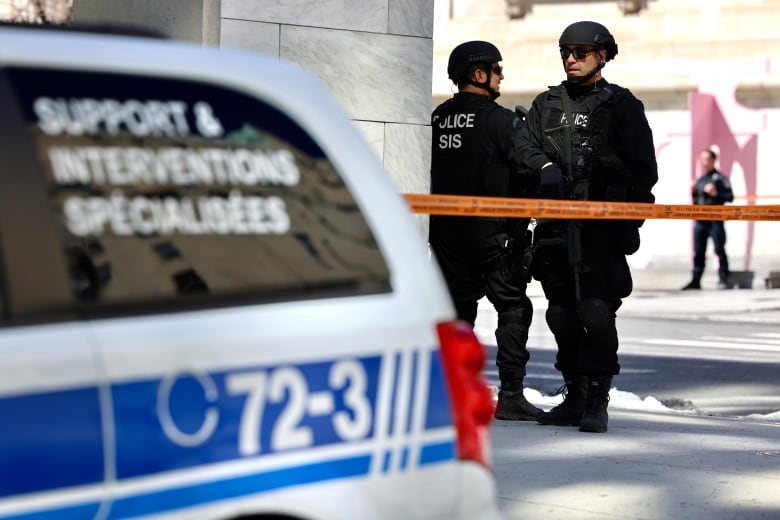 Two police officers from the force's special intervention team stand behind police tape. 