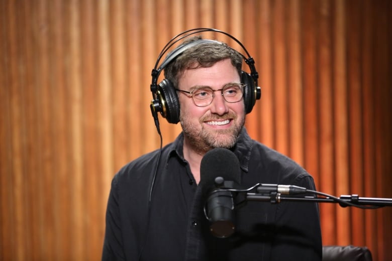 Nick Green smiling, wearing headphones and sitting in front of a studio microphone.