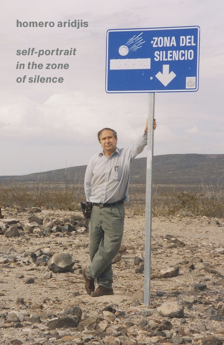 A man stands next to a sign in the desert. 