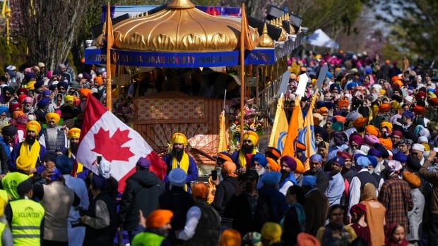 Hundreds of people march on a city street with orange flags. A Canadian flag is also visible.