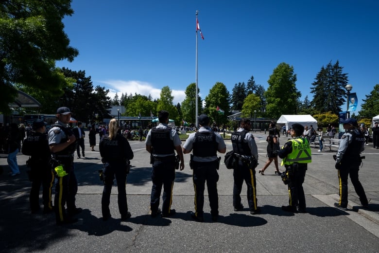 Eight RCMP officers, some wearing baseball caps, stand in a paved courtyard.