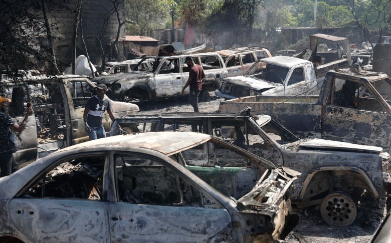 People walk among a number of burned out cars.