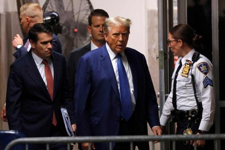 A man in a blue suit stands between an officer and another man in a suit. 