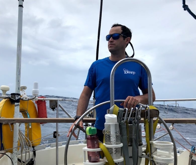 A man stands on a boat, out at sea.