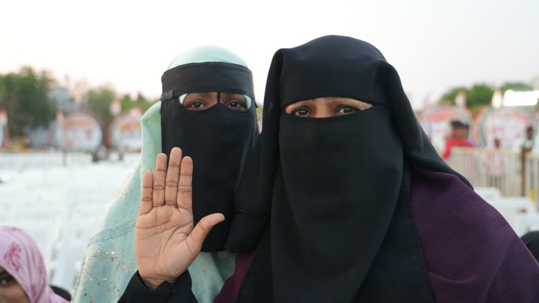 Two women pose for the camera. The woman on the right holds her hand up.