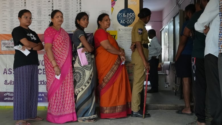 Five women line up to vote. They each hold a paper ballot in their hands.