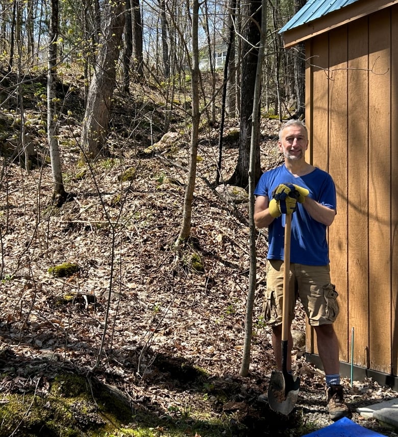 A man stands in the woods holding a shovel.