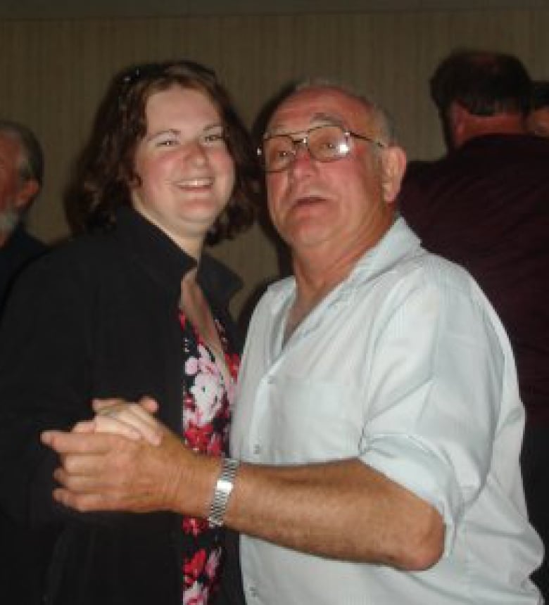 A smiling woman dances with an older man wearing glasses.