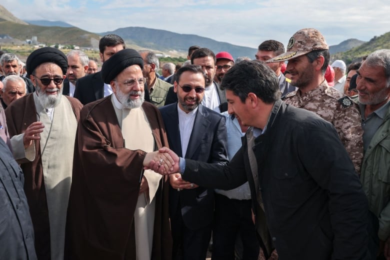 Two men shake hands while others watch.