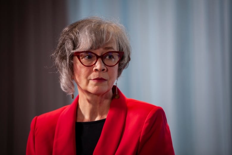 A woman in red coat and a winged pair of glasses is pictured during a press conference.