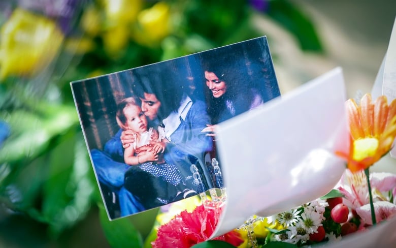 A photo of a man, woman and baby, which appears to be decades old, is shown in closeup beside a bouquet of flowers.