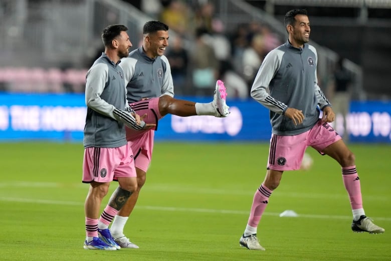 Three players wearing pink exercise on a soccer pitch.