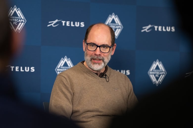 A white man wearing a sweater speaks during a news conference.