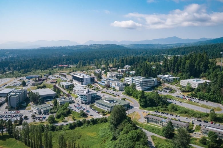 An aerial picture of a university campus, with various buildings surrounded by green forests and mountains.