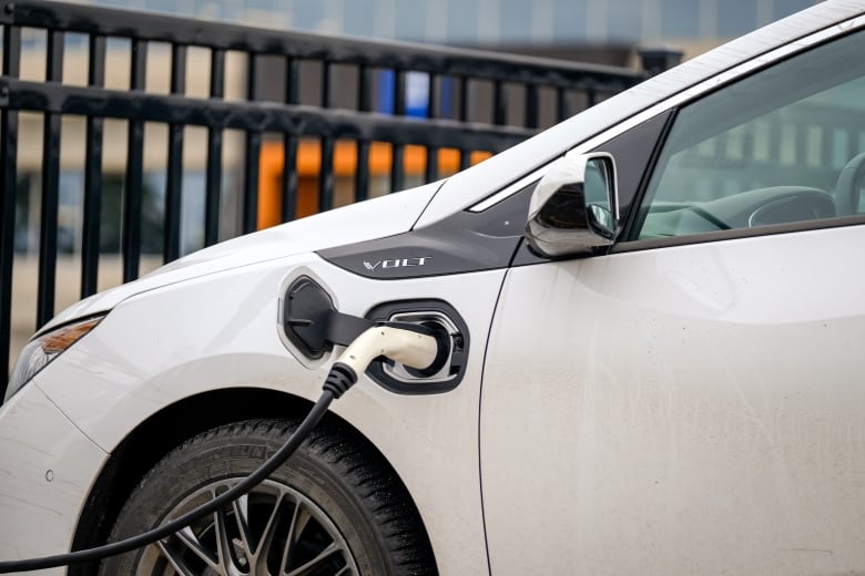 A charger is plugged into the side of a white electric vehicle.