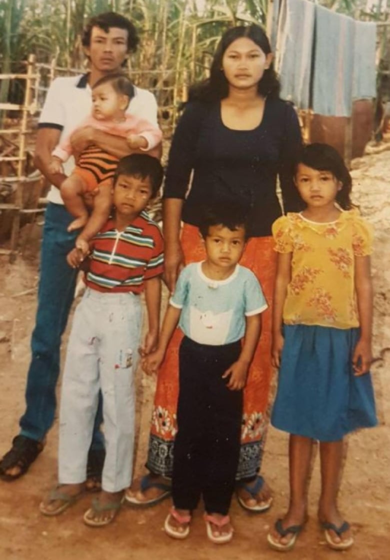 A family of five, including three children and a baby held in a man at the right's arms, look at the camera, with a line of laundry seen behind them drying in the air.