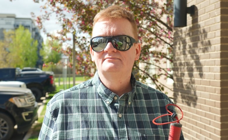 A man with sunglasses stands in front of an apartment building. 